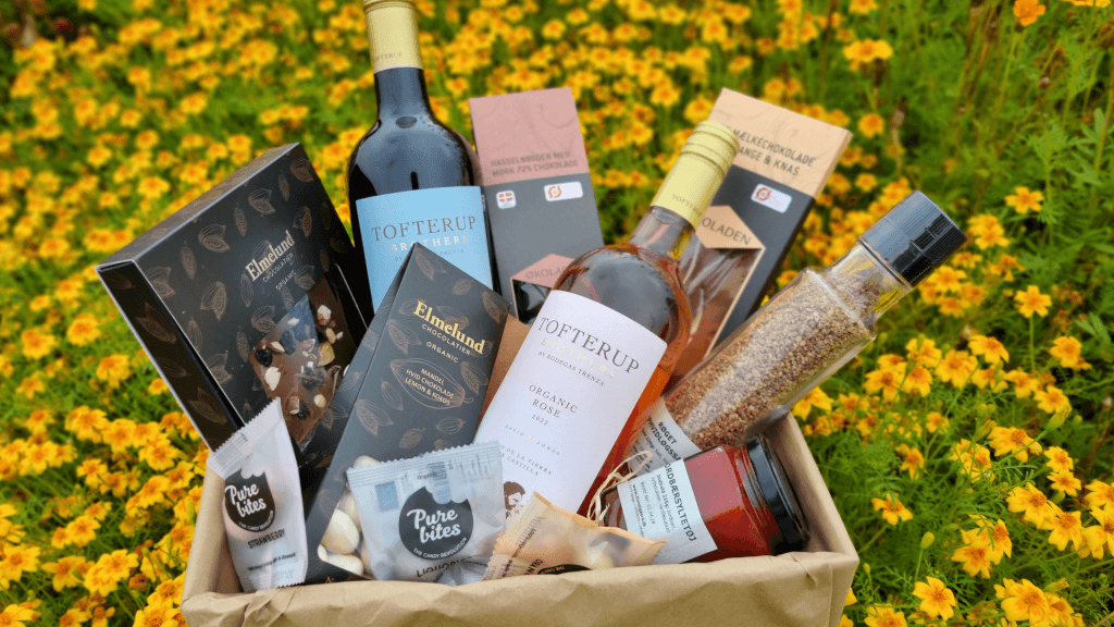 Ein Geschenkkorb mit Spezialitäten aus dem Hofladen von Tinnetgaard liegt auf einer Blumenwiese